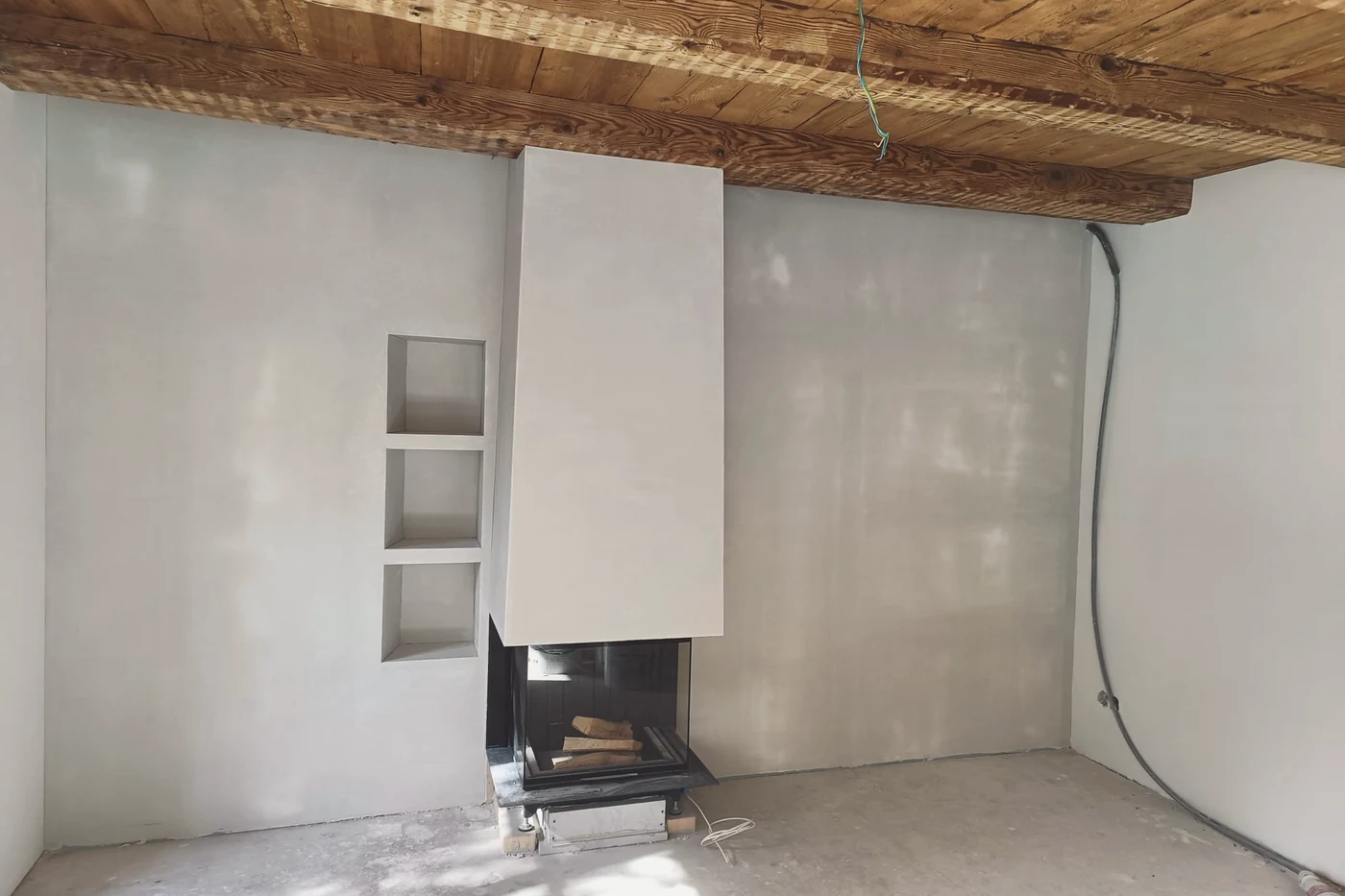 Wohnraum mit Cheminée, die Wände frisch verputzt, darüber eine Holzdecke