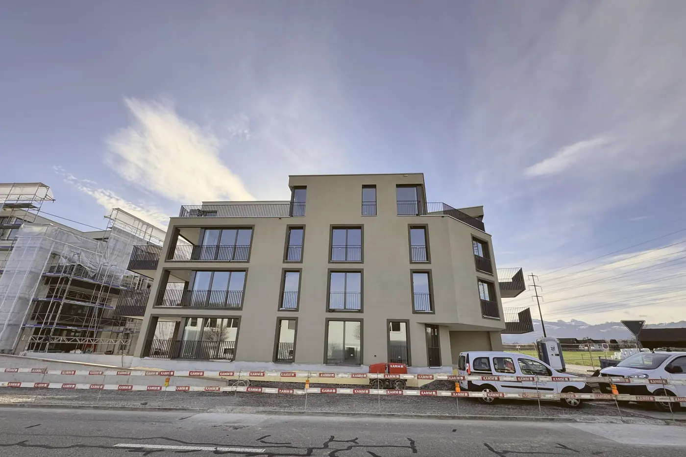 Neubau mit heller Fassade unter blauem Himmel, davor die Baustellenabschrankung