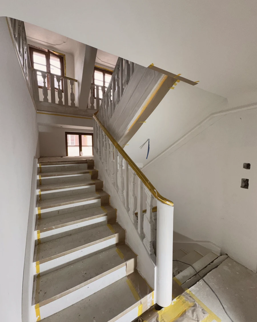 Treppe mit weissem Geländer in einem renovierten Altbau, Stufen noch abgedeckt
