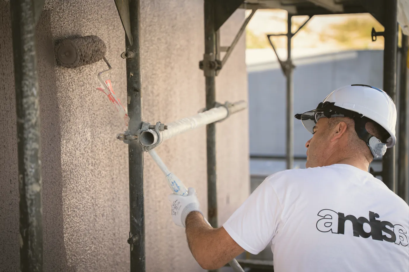 Maler im Andisa-Shirt streicht eine Fassade, Logo auf dem Rücken