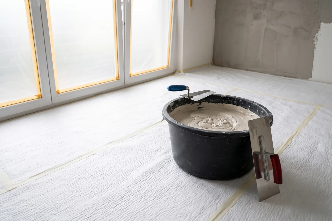 Mörtelkübel mit frischem Putz, Berner Putzkelle und Glättekelle auf dem Floorliner