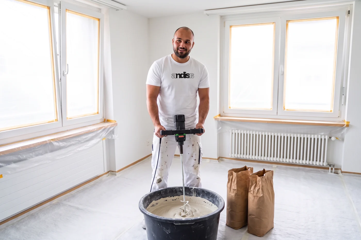 Gipser im Andisa-Shirt mischt Putz mit dem Rührwerk im Mörtelkübel an