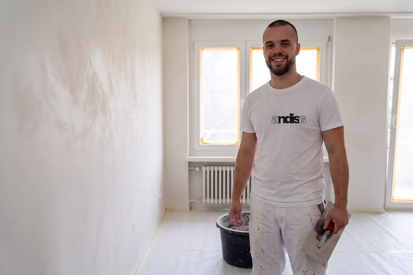 Gipser im Andisa-Shirt mit der Glättekelle neben einer frischen Kalkputzwand