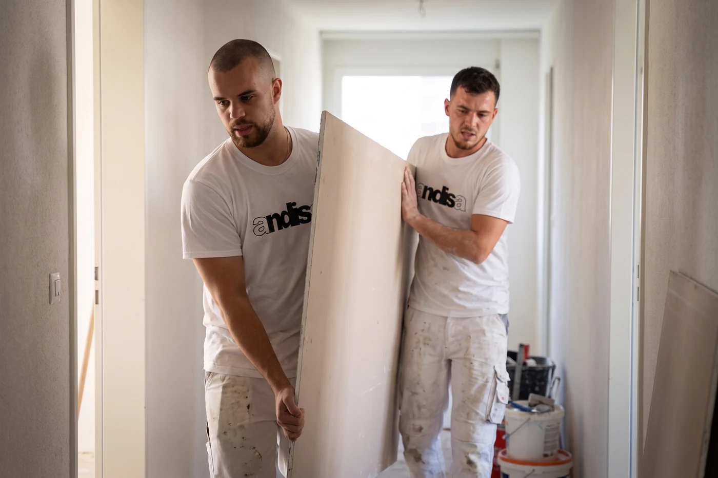 Zwei Andisa-Mitarbeiter tragen eine Gipsplatte durch eine Wohnung
